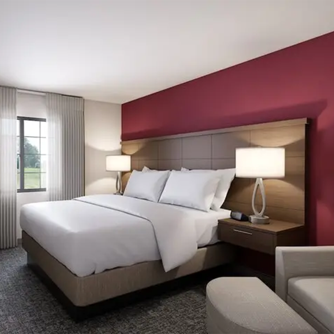 Hotel room pic with red accent wall, recliner seat and king bed.