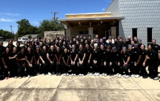 Group photo of doctors in navy blue scrubs standing together outside a medical facility.
